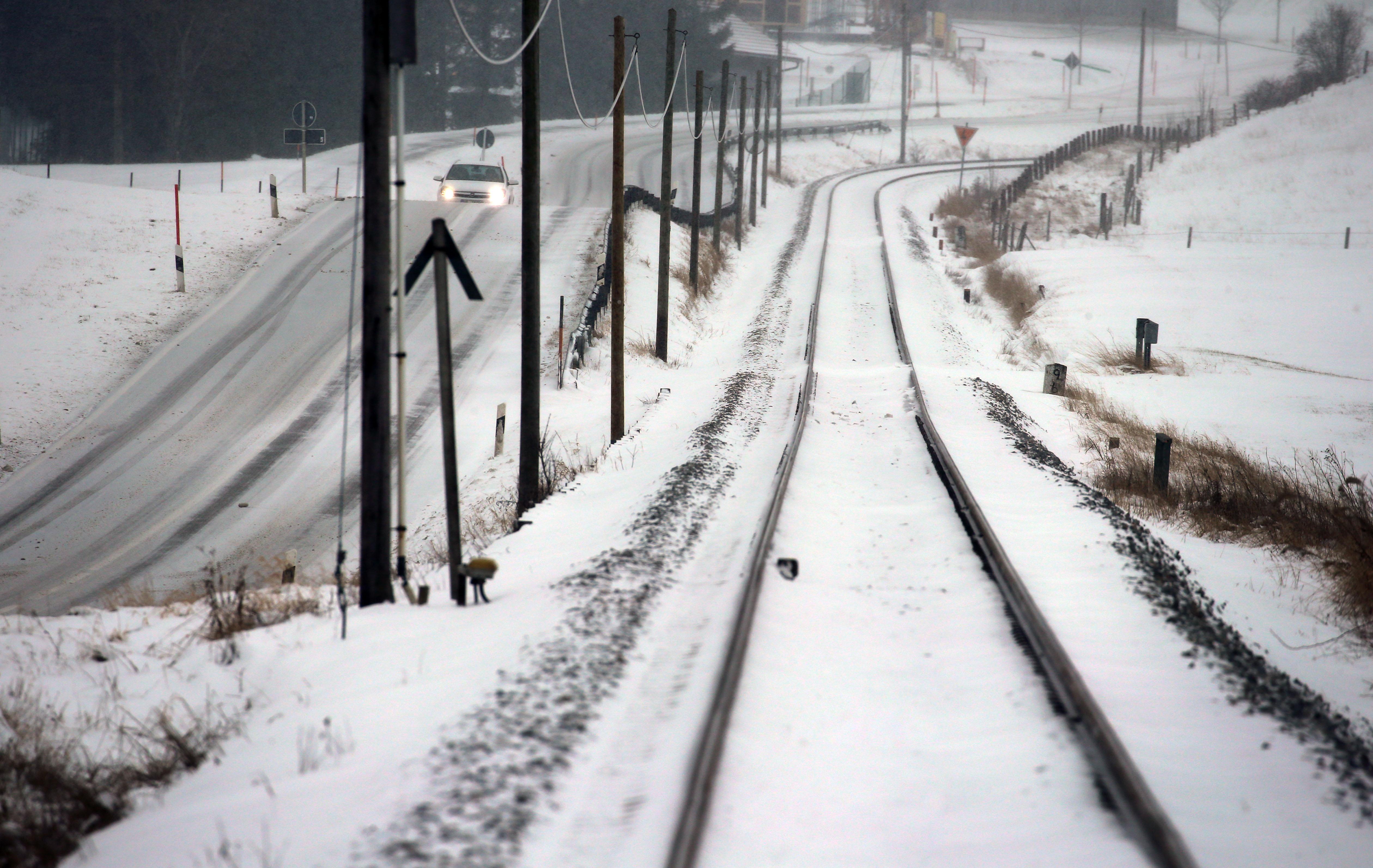 Eine weiße Schneedecke legt sich sowohl auf die Straße neben den Schienen, als auch über die Gleise der Bahnstrecke Füssen-Buchloe.