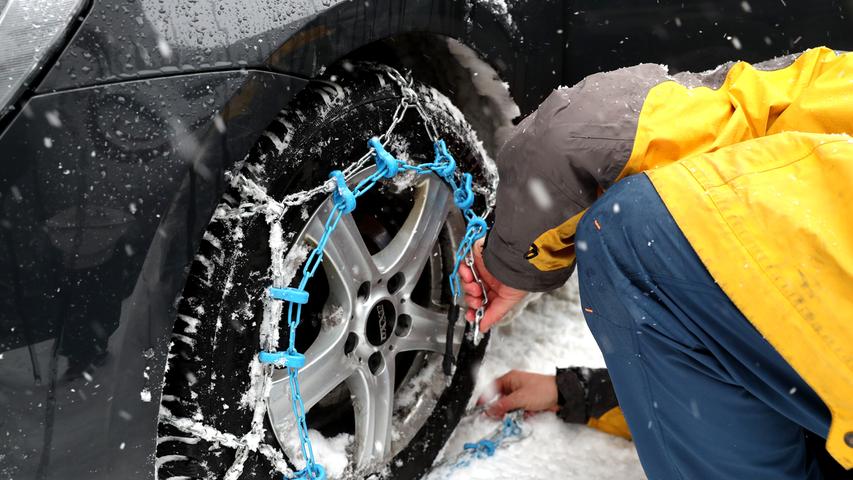 Ein Mann bringt im Salzburger Land Schneeketten an seinem Auto an.