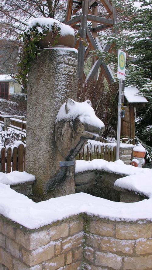 Wolf mit Schneehaube: Der Brunnen in der Dorfmitte von Wolfsbronn.