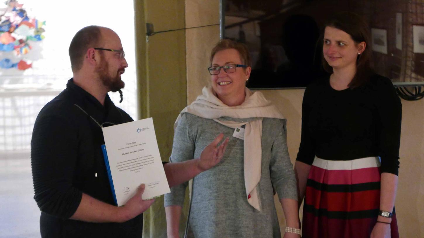 Susanne Mäckl und Sabine Fink nehmen von Simon Hamper (v. r.) den Förderpreis des Landesverbandes Museumspädagogik Bayern e.V. entgegen.