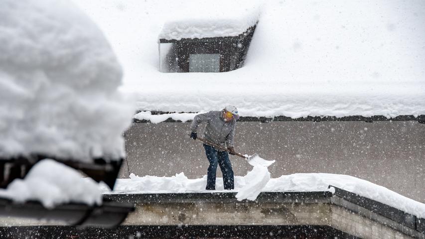 Ein Mann schaufelt im bayerischen Elisabethszell Schnee von einem Dach.