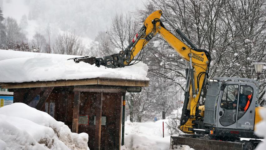 In Oberstdorf wird der Schnee per Bagger vom Dach einer Bushaltestelle geräumt.