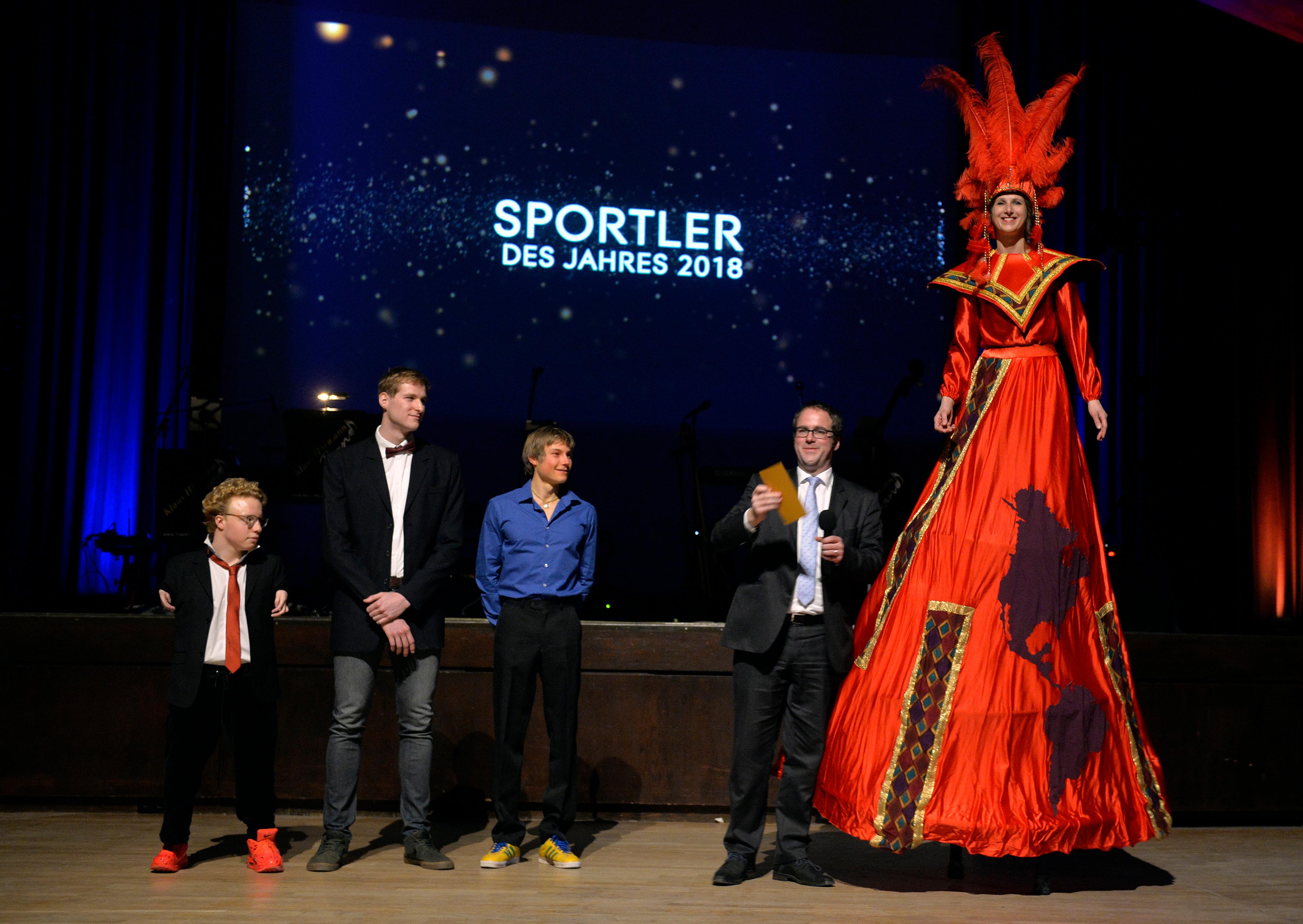 Bei der offiziellen Verkündung brachte eine Stelzenläuferin des Münchner Sporttheaters den Umschlag mit dem Ergebnis. Erlangens Oberbürgermeister Florian Janik (2. von rechts) nahm den Brief entgegen.