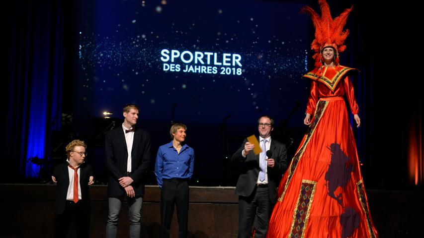 Bei der offiziellen Verkündung brachte eine Stelzenläuferin des Münchner Sporttheaters den Umschlag mit dem Ergebnis. Erlangens Oberbürgermeister Florian Janik (2. von rechts) nahm den Brief entgegen.