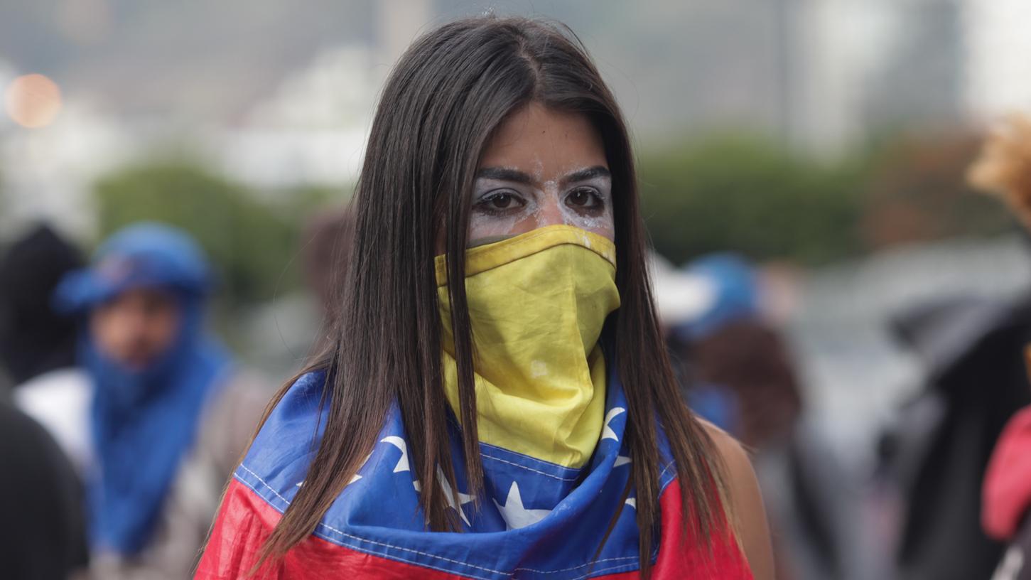 Eine Frau hat sich mit einer venezolanischen Flagge maskiert und protestiert gegen den Präsidenten Maduro. Parlamentspräsident Guaidó hat die sozialistische Regierung von Maduro für entmachtet erklärt und sich selbst zum Übergangs-Staatschef ausgerufen.