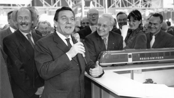 Immer wieder brachte die Spielwarenmesse politische Gegner zusammmen. Das zeigt das Foto von 2001 mit SPD-Kanzler Gerhard Schröder (mit Mikro) und dem CSU-Ministerpräsidenten Edmund Stoiber (re. daneben). Zur 52. Spielwarenmesse hatte sich die Politprominenz am Stand von Piko-Modelleisenbahnen aufgestellt und schwelgte amüsiert in Erinnerungen an ihre erste eigene Spielzeugeisenbahn. Bei der Bundestagswahl im Jahr darauf waren beide Männer dann wieder Kontrahenten im Kampf um die Kanzlerschaft.