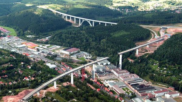 Die Haseltalbrücke (im Vordergrund) ragt als eine der 17 Großbrücken auf thüringischer Seite heraus; es handelt sich dabei um die erste südlich des Autobahndreiecks Suhl. Das Bauwerk, eine mehr als 800 Meter lange Balkenbrücke, überspannt den Suhler Ortsteil Heinrichs mit den ehemaligen Werksanlagen des Fahrzeugwerks Simson.