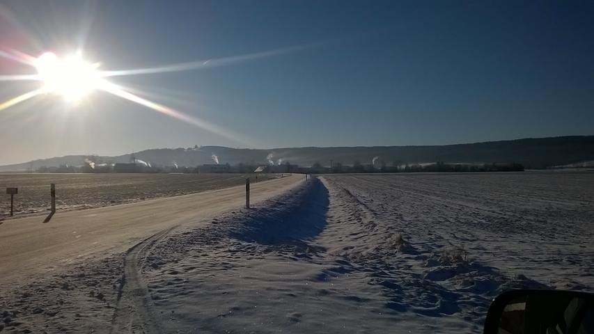 Die Sonnenstrahlen bringen den Schnee zum Glitzern. Im Hintergrund sind die rauchenden Schornsteine von Sammenheim zu sehen.