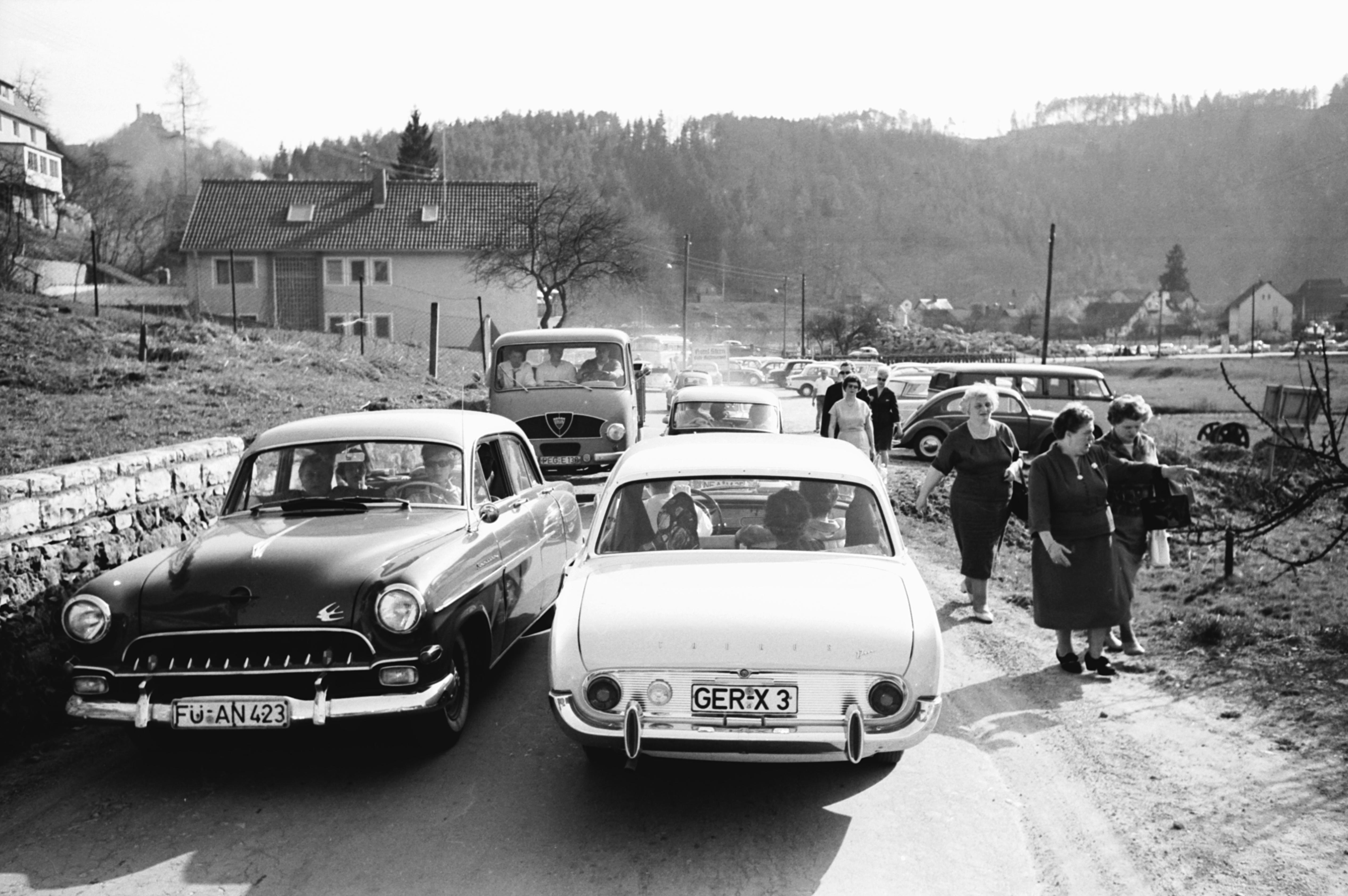 Damals, als Ford und Opel noch Autos der oberen Mittelklasse bauten... Vorne im Bild kommen sich gerade ein Ford Taunus 17m - Spitzname "Badewanne" - und ein Opel Kapitän (der ab 1964 sogar den Aufstieg in die automobile Oberklasse schaffte) entgegen. Der Lieferwagen links im Hintergrund ist ein damals schon rarer Faun F24. Wanderer hatten es an den Osterfeiertagen anno 1962 übrigens nicht ganz leicht: Oft wurden sie - wie hier bei Behringersmühle in der Fränkischen Schweiz - hart an den Straßenrand gedrängt und mit Staub bedeckt.