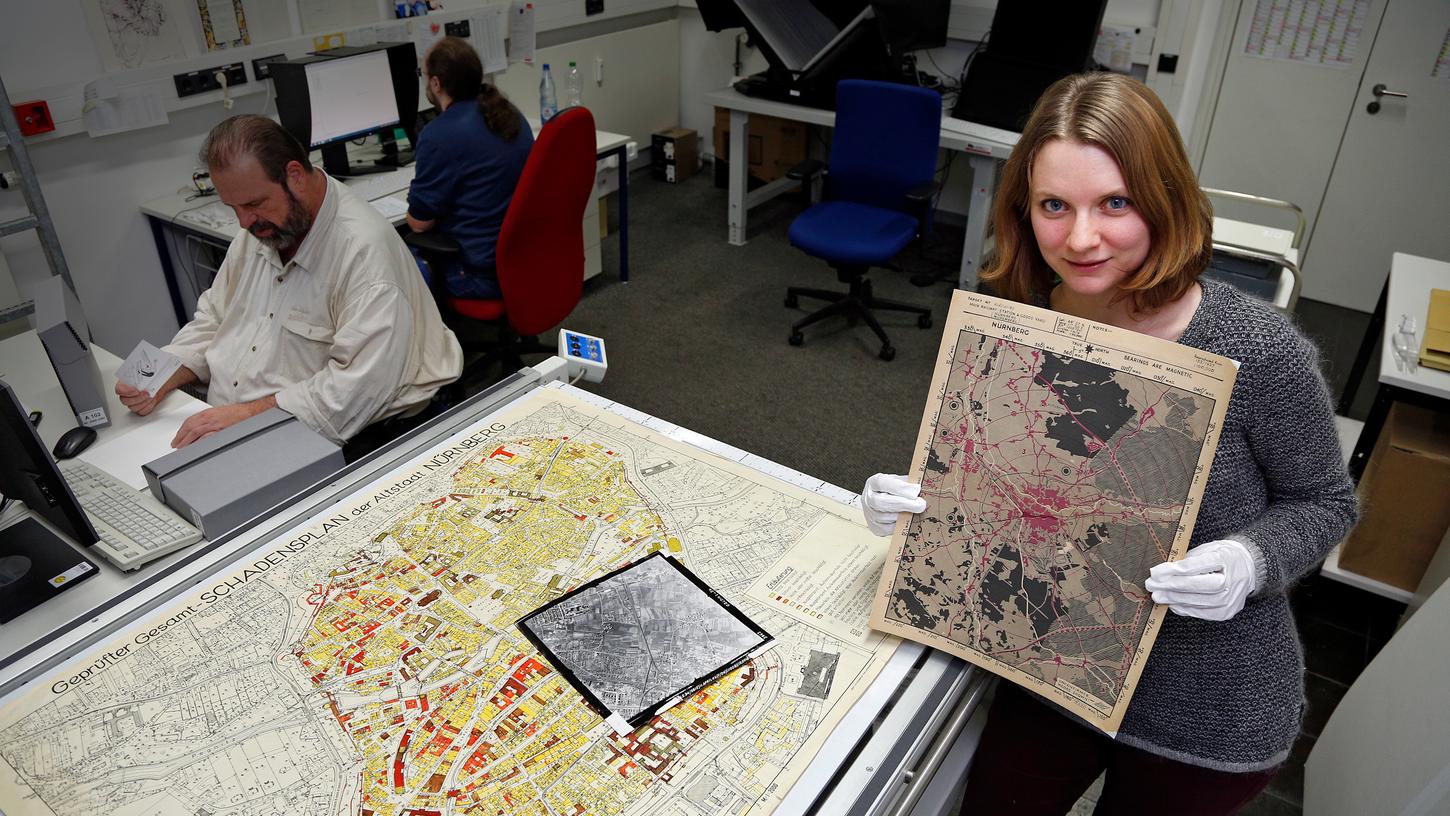 Antonia Landois vom Stadtarchiv zeigt eine "Zielkarte" der Alliierten aus dem Zweiten Weltkrieg. Auf dem Tisch liegt eine Schadenskarte der Stadt, welche Kriegszerstörungen dokumentiert, und ein Luftbild der Alliierten.