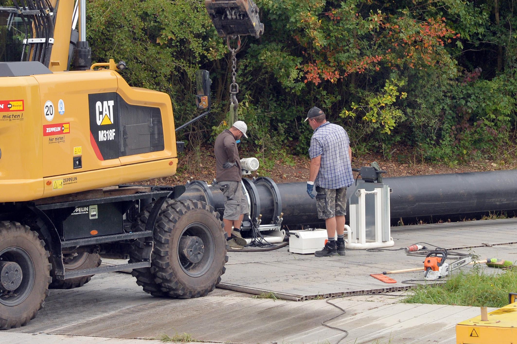 Mehrere Arbeiter sind tagsüber an den großen Rohren zugange.