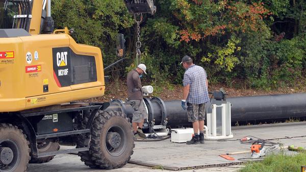 Mehrere Arbeiter sind tagsüber an den großen Rohren zugange.