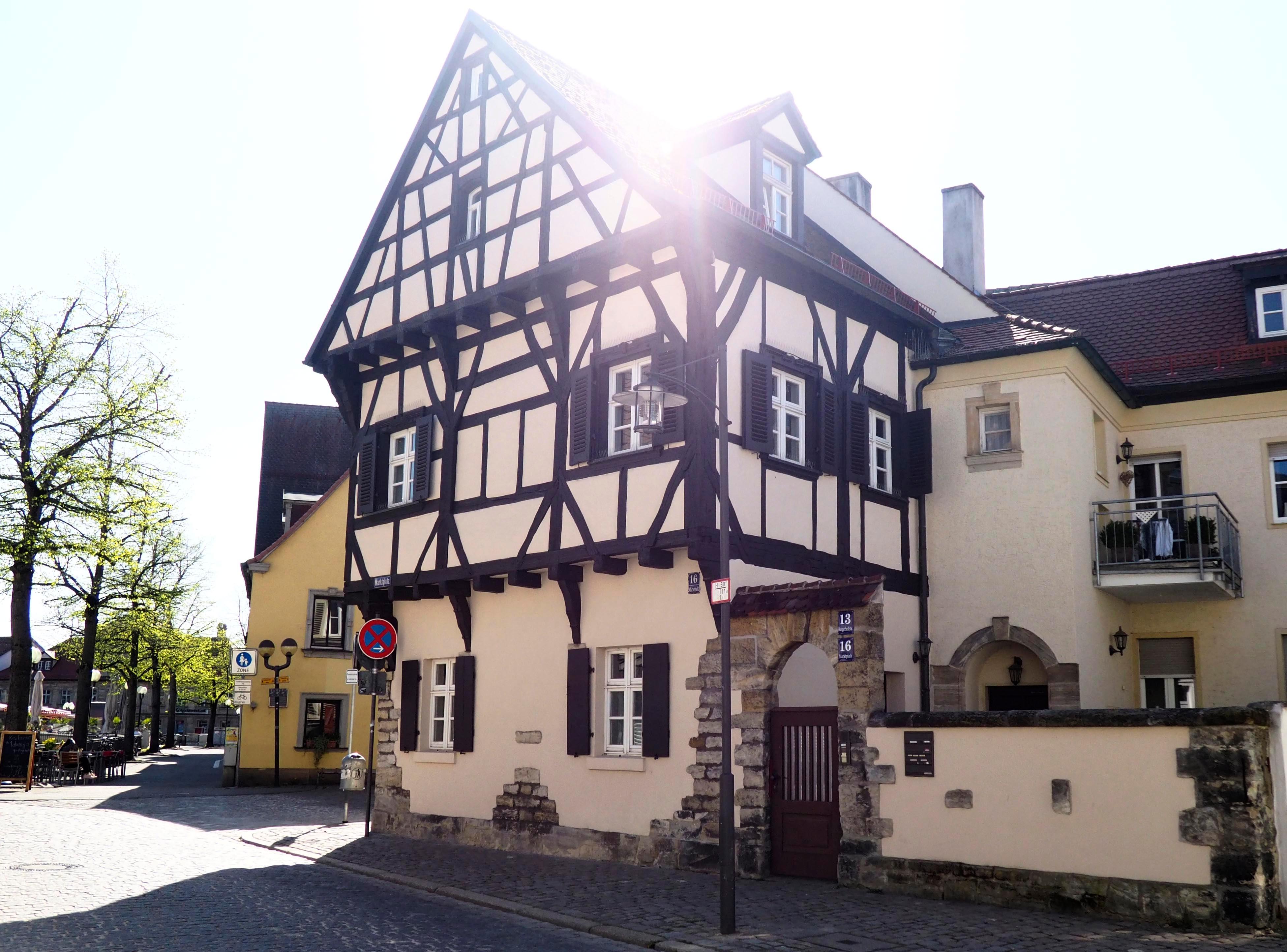 Das Haus am Marktplatz 16 wurde 1392 errichtet - mit einem oberen, vorragenden Stockwerk. 1619 taucht es in Unterlagen als „das hohe Hauß“ auf. Der Forchheimer Maler Michael Kotz hielt das Wohnhaus um 1900 in einer aquarellierten Federzeichnung fest. Bis heute hat der zweistöckige Fachwerkbau seinen Stammplatz als Eckhaus an der Burgerhofstraße behalten.
