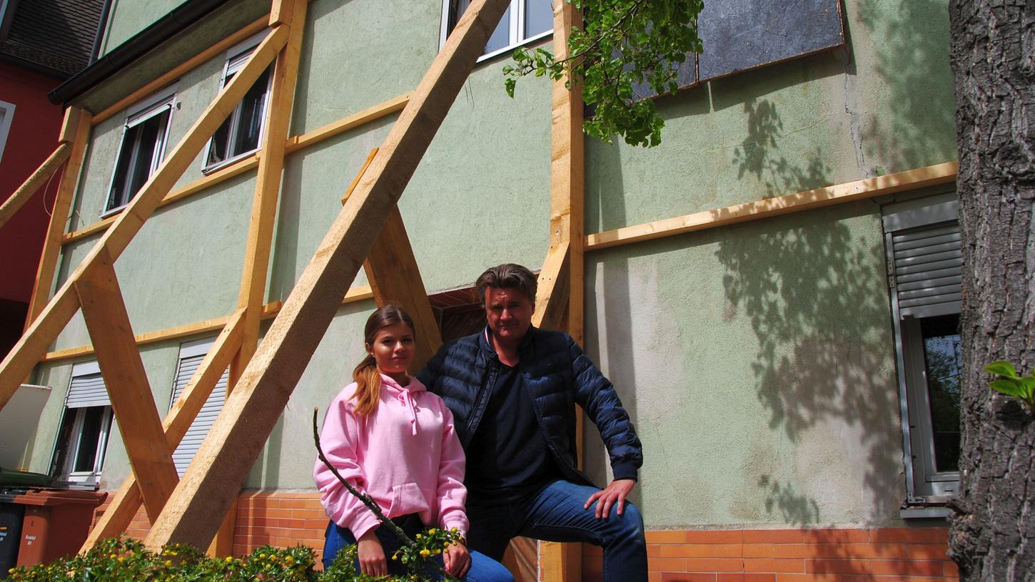 Laura und Alexander Messner von der Firma HG Bau vor dem Haus in der Wöhrwiese 8, das derzeit innen wie außen von Holzgerüsten gestützt wird. Oben rechts ist das mit Pressspan abgedeckte Loch in der Außenwand zu erkennen.