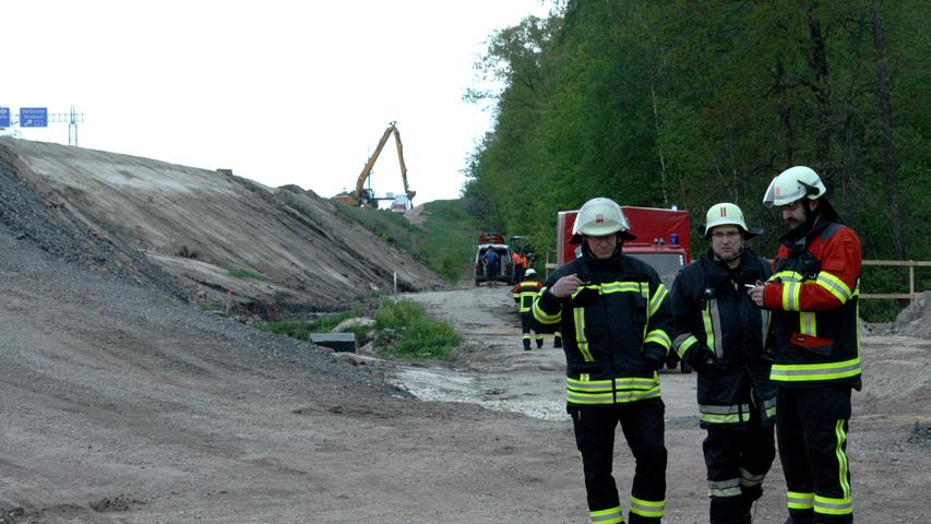 Lagebesprechung der Feuerwehrführung im Hintergrund der Fundort der Bombe. Oben auf dem Damm der A73 wird inzwischen an der Baustelle weitergearbeitet, auch der Verkehr fließt zu diesem Zeitpunkt noch.