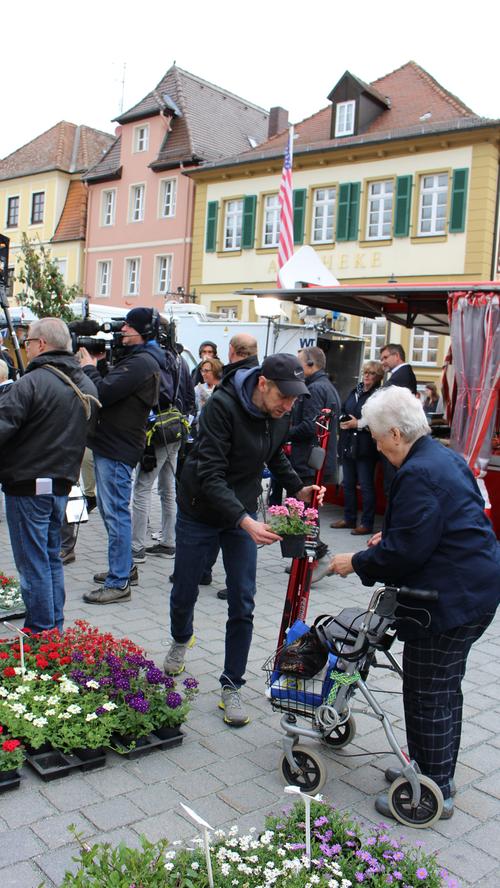 Nebenbei hilft ein Mann aus dem Fernsehteam einer Wochenmarktbesucherin bei der Wahl der Blumen.