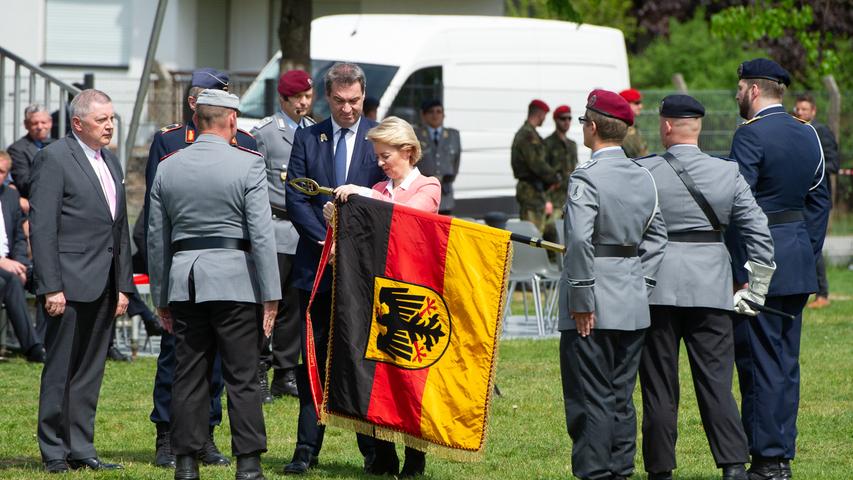 Ursula von der Leyen (CDU, M), Bundesverteidigungsministerin, bindet neben Markus Söder (CSU, l), Ministerpräsident von Bayern, im Stadtpark in Roth anlässlich der Indienststellung des Landesregimentes Bayern für den Heimatschutz ein Fahnenband an die Truppenfahne.