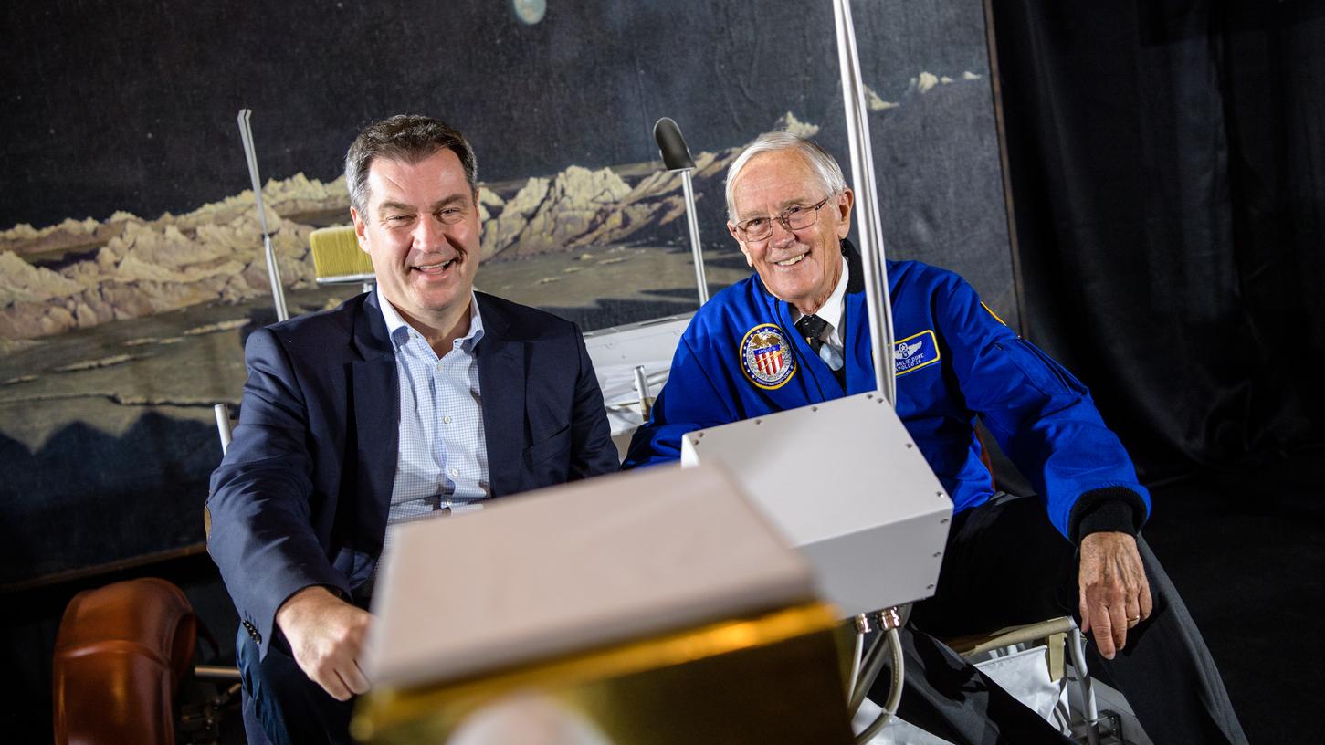 Markus Söder (links) und Charlie Duke, ehemaliger US-Astronaut, sitzen auf einem Nachbau eines Mondautos.