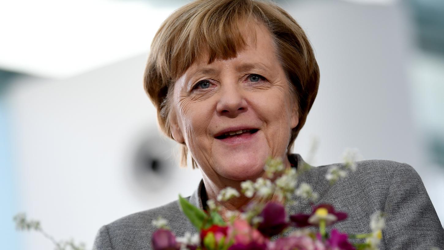 Bundeskanzlerin Angela Merkel (CDU) freut sich über einen Blumenstrauß. Sie feiert am Mittwoch ihren 65. Geburtstag.