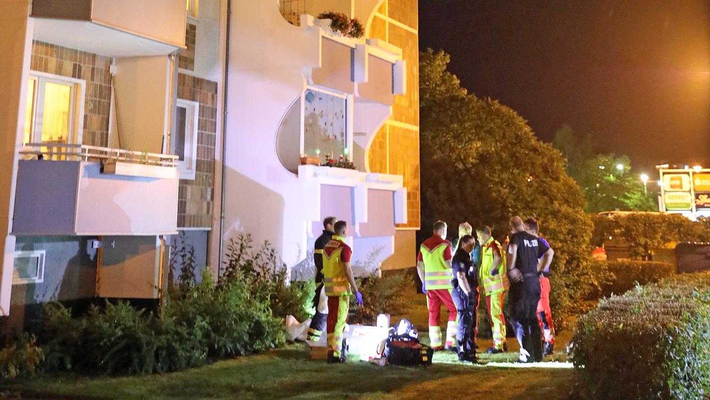 Rostock: Polizisten, Feuerwehrleute und Anwohner stehen vor einem Hochhaus, in dem ein Mann zuvor auf einen Säugling eingestochen hatte und dann über die Balkonbrüstung geklettert war, um in die Tiefe zu springen.