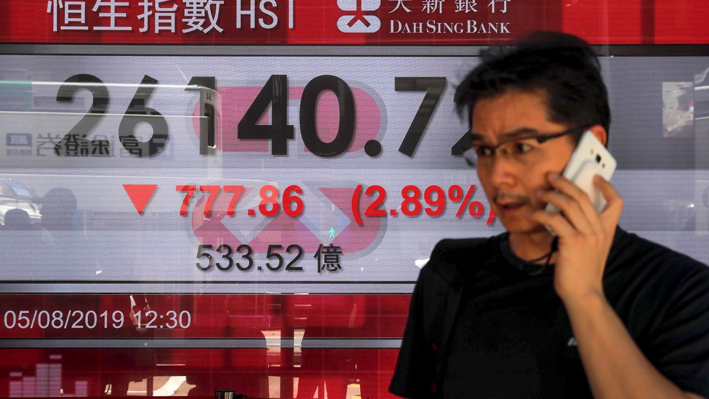 Ein Mann telefoniert vor einer Anzeigetafel, die den Aktienindex der Hong Kong Composite Index anzeigt. Die asiatischen Märkte reagierten zu Beginn der Woche auf die Eskalation im Handelskrieg zwischen den USA und China.