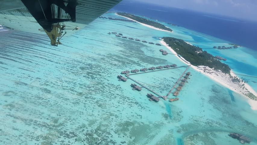 Sonderbare Welt, sonderbares Land: Von der Luft aus sieht man, was die Malediven ausmacht. Kleine Inseln, die ein Hausriff aus Korallen (heller Teil des Meeres) direkt umgibt. Dort, wo das Meer dunkler scheint, beginnt das Außenriff und damit das Meer mit ordentlich Tiefgang.
