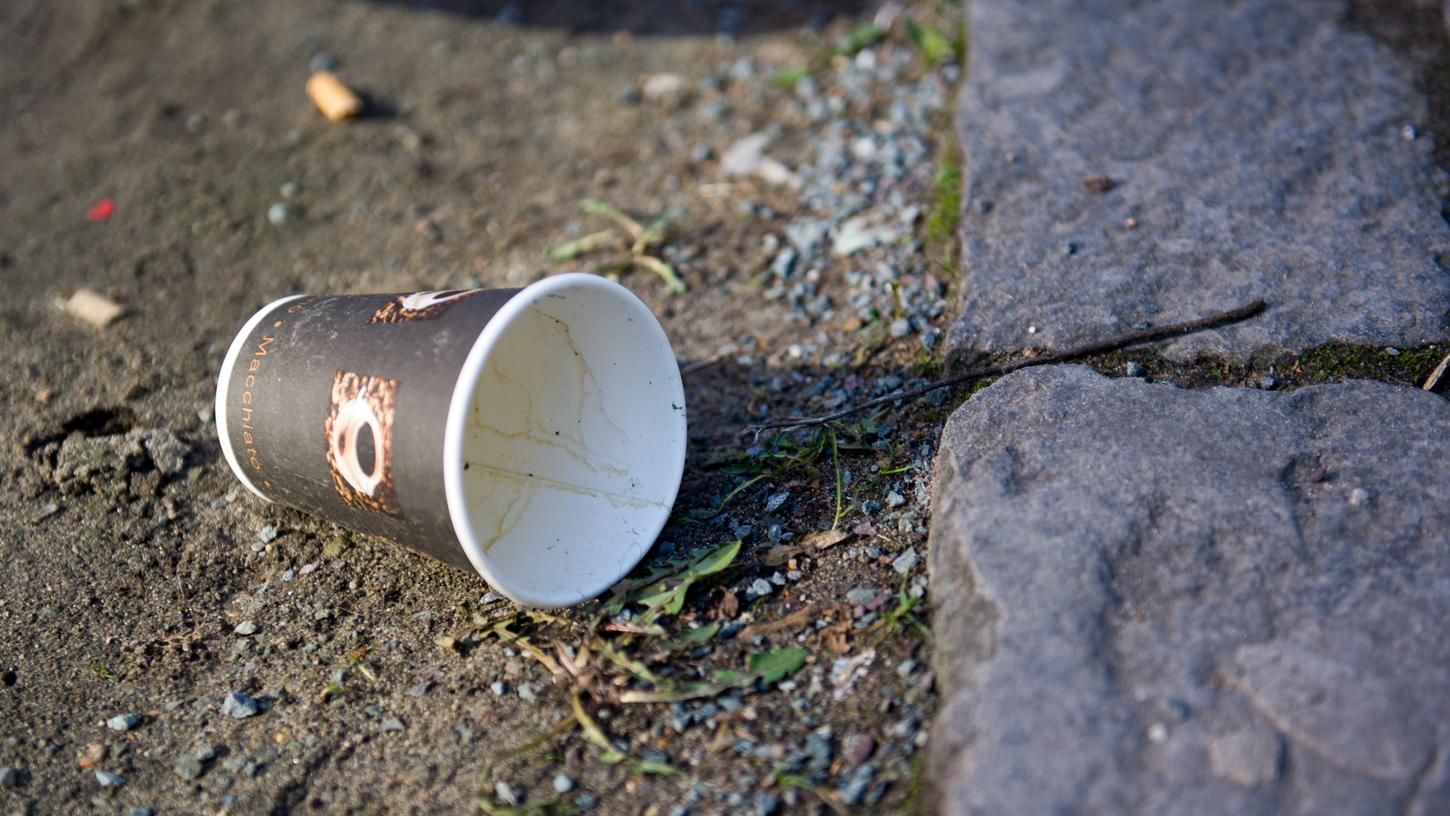 Ein leerer Kaffeebecher liegt auf dem Boden. Hersteller von Wegwerfartikeln wie Zigaretten oder Kaffeebecher sollen in Zukunft die Kosten fürs Sauberhalten von Straßen und Parks mittragen.