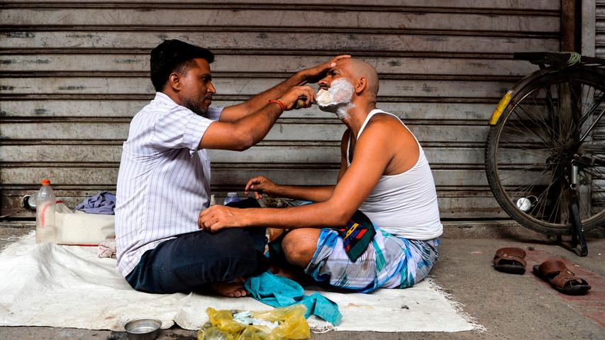 In der indischen Hauptstadt Neu Dehlhi geht das Leben trotz Kaschmir-Krise seinen Gang. Ein Barbier rasiert einen Kunden am Straßenrand.