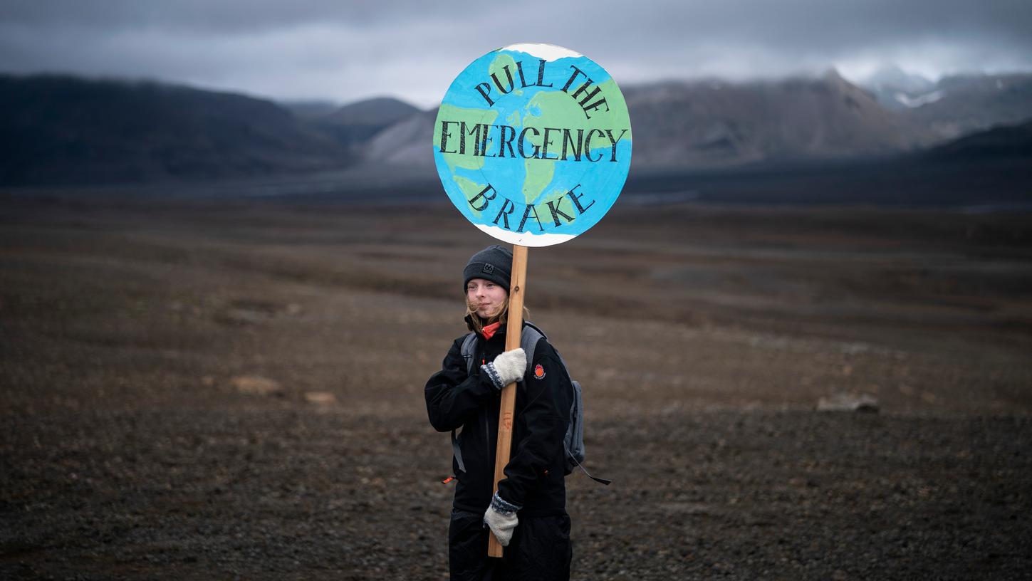 Ein Mädchen hält ein Schild mit der Aufschrift "Zieh die Notbremse" (Pull the Emergency Brake) während sie über das Geröll des Okjökull zu einer Gedenkveranstaltung für den vergangenen Gletscher wandert.