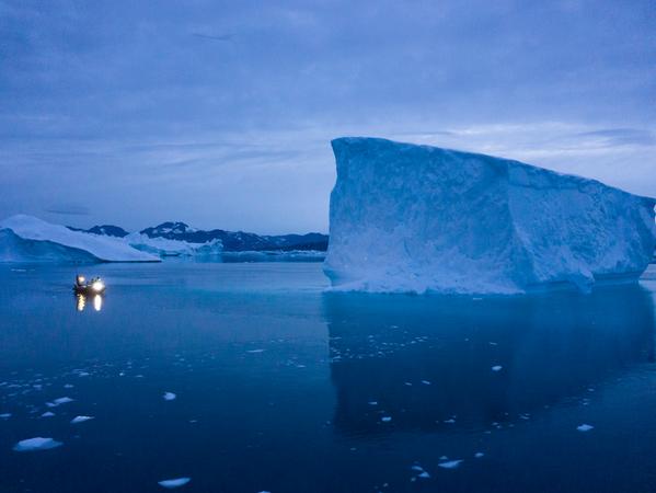 Dieses Schiff umfährt in der Abenddämmerung einen Eisberg in Grönland.
