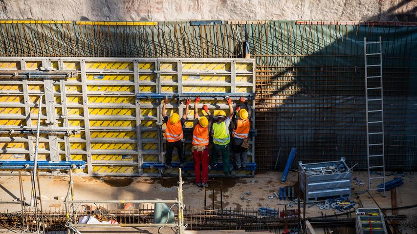 Bauarbeiter bringen die Stahlbewehrung und Verschalungen für die Betonwände in der Baugrube hinter dem historischen Rundbau an.