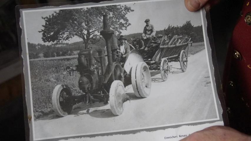 Ein Schwarz-Weiß-Foto, das einen alten Schlepper zeigt, der unter anderem zum Ziehen einer Dreschmaschine genutzt wurde. Hierfür konnte eines der vorderen Räder abmontiert werden. Mit einem Riemen wurde dann die Dreschmaschine angetrieben.