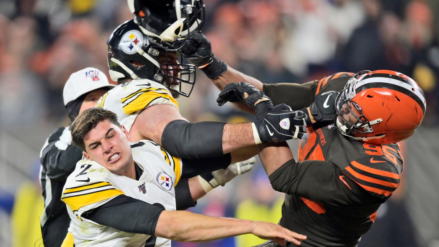 Cleveland Browns Defensiv-Spieler Myles Garrett (r) hält den Helm von Pittsburgh Steelers Quarterback Mason Rudolph (vorne l) in der Hand und schlägt ihn damit.