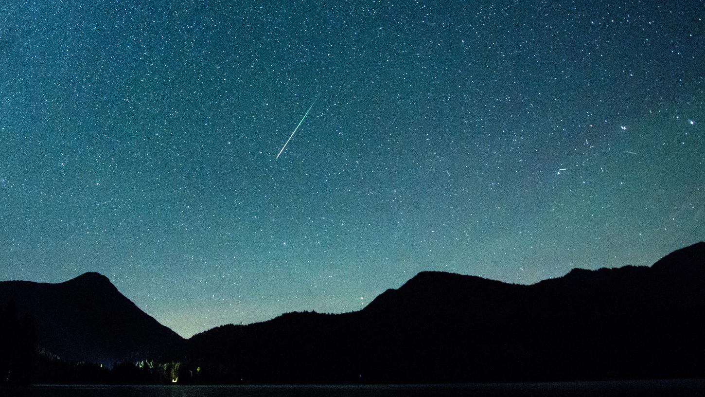 Eine Sternschnuppe leuchtet vor der Milchstraße am Himmel über dem Walchensee.