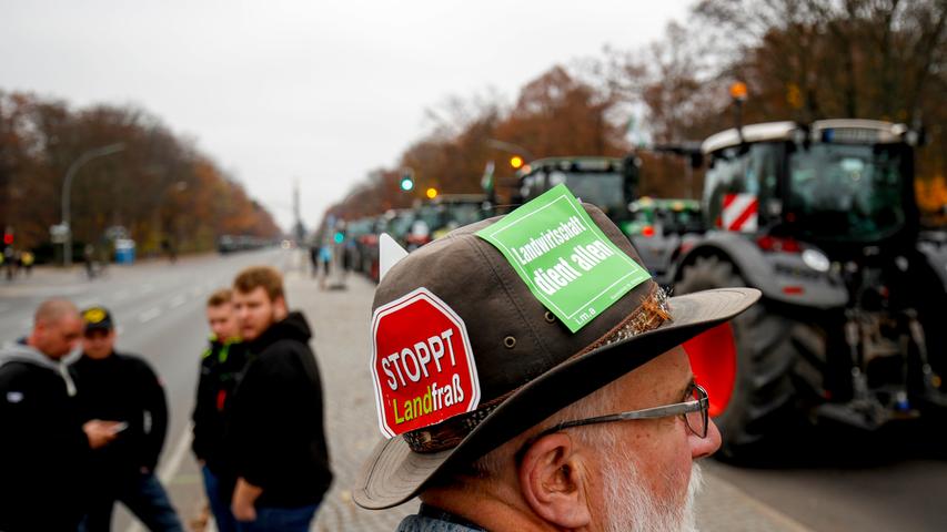 A protestor wears a hat bearing stickers reading "Stop eating our land" and "Agriculture serves all" as he stands next to a long row of farmers lining up with their tractors along "Strasse des 17. Juni" Avenue during a protest on November 26, 2019 in Berlin against the German government's agricultural policy including plans to phase out glyphosate pesticides and to implement more animal protection. (Photo by Odd Andersen / AFP)