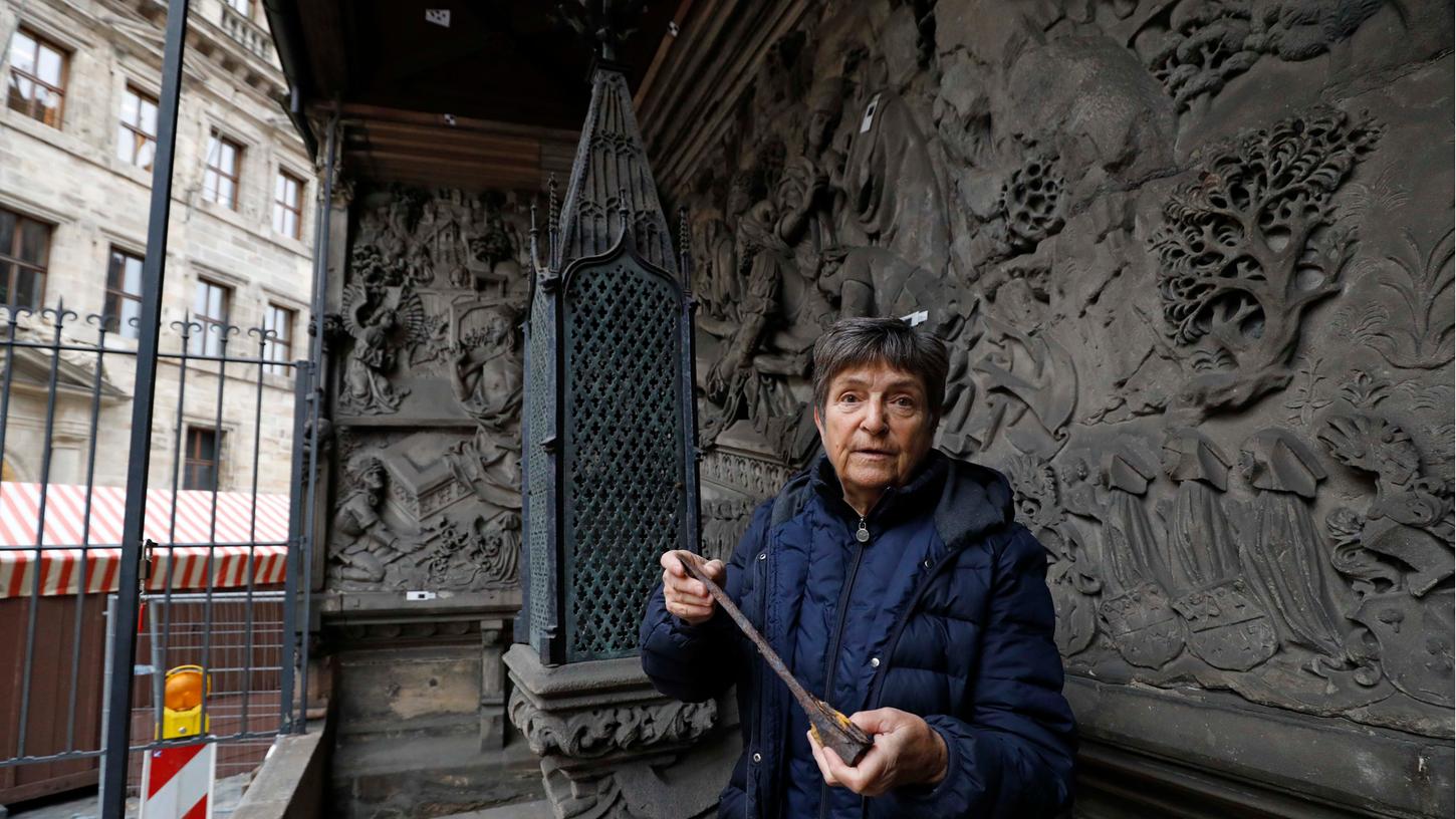 Architektin Alexandra Fritsch hat das Absperrgitter geöffnet und steht an der Grabstätte der Stifter. Das Epitaph an der Außenwand von St. Sebald ist äußerst kunstvoll gearbeitet. Adam Kraft hat auch Details wie Bäume mit besonderer Sorgfalt gestaltet.