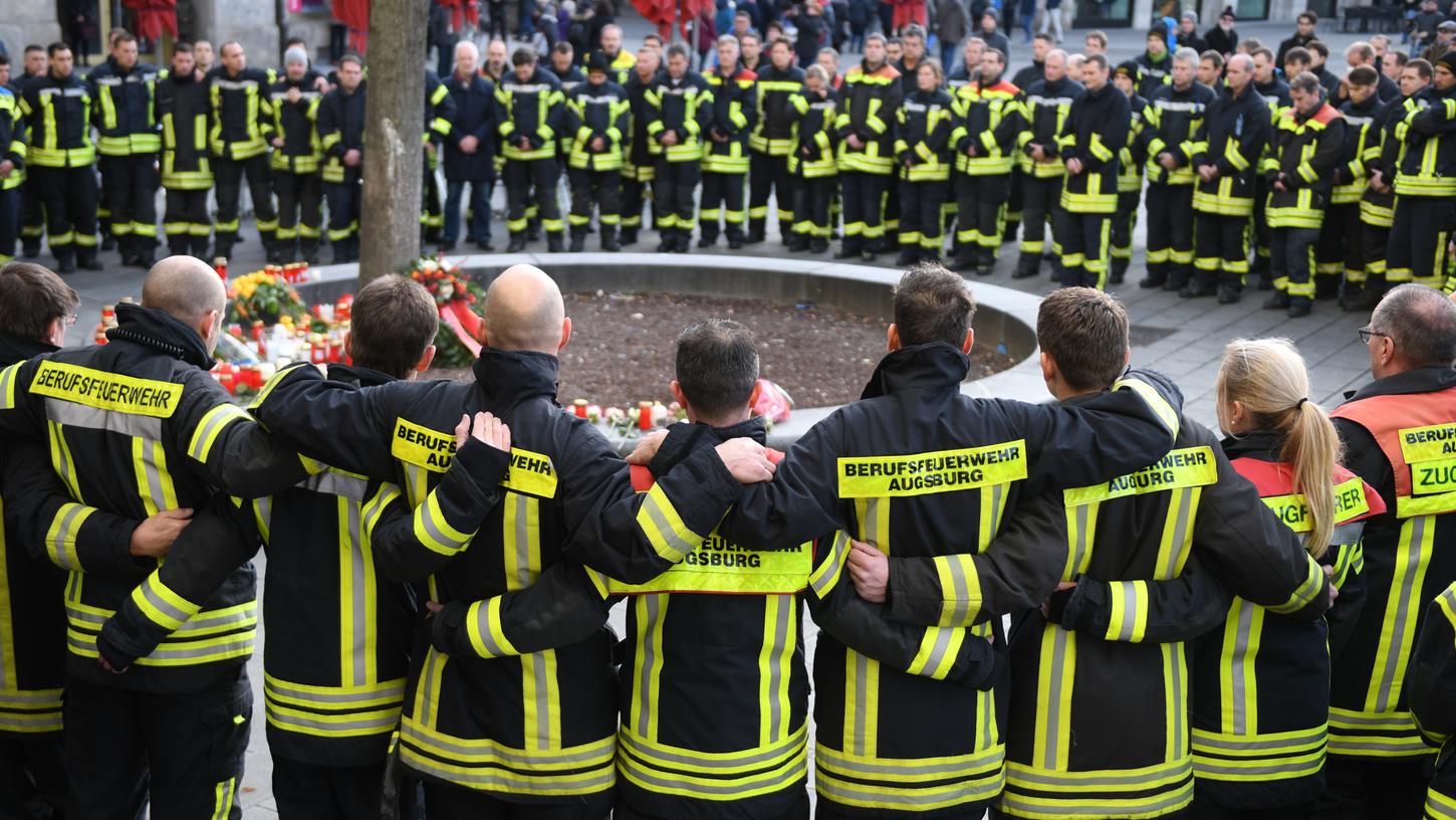 Am Königsplatz in Augsburg trauern Feuerwehrmänner um ihren Kameraden. Der 49-Jährige war am Freitagabend in seiner Freizeit in einer Auseinandersetzung mit einer Gruppe so schwer verletzt worden, dass er starb.