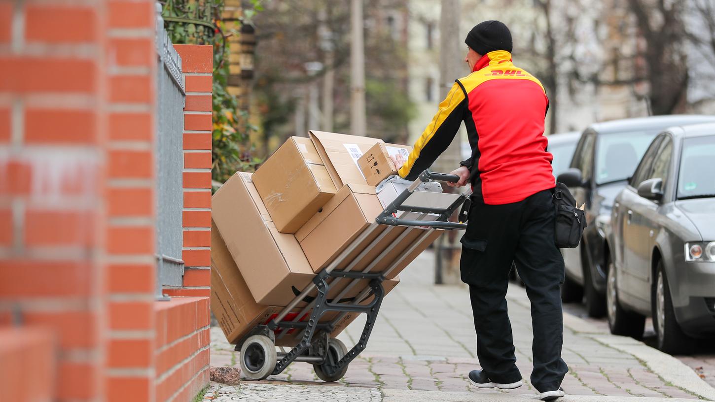  Ein DHL-Paketzusteller geht mit einer Sackkarre voll Pakete zu einem Haus