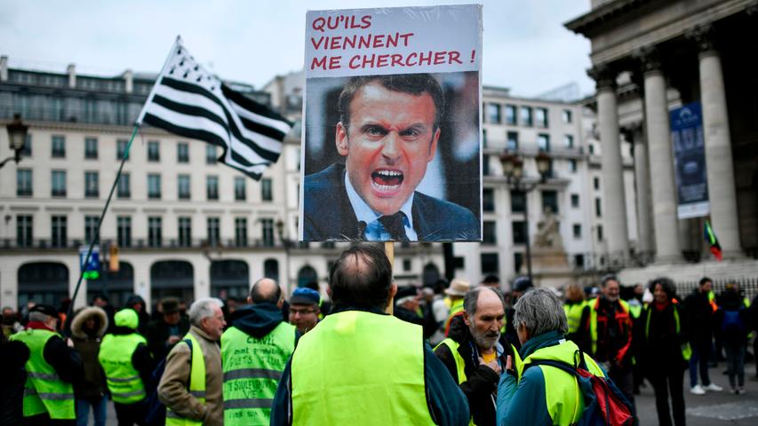 Demonstranten der Gelbwesten-Bewegung sind am 28. Dezember wieder auf Frankreichs Straßen unterwegs. Auf dem Schild mit dem französischen Präsidenten steht "Lass sie kommen und mich holen!". Die Gelbwesten streiken auf dem Place de la Bourse in Paris gegen die Rentenüberholung der französischen Regierung.