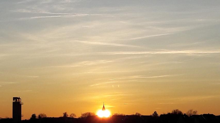 Wie zwei glühende Augen geht die Sonne hinter der St.-Nikolai-Kirche in Neuendettelsau unter.