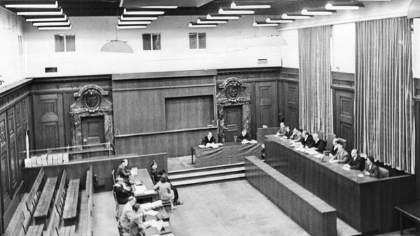 Wer vor der Schwurgerichtskammer steht, hat eine hohe Strafe zu erwarten, die Angeklagten müssen sicher untergebracht werden – daher wird der "Schwurgerichtssaal meist in einem rückwärts liegenden Mittelbau oder in einem Seitenflügel angeordnet", so das "Handbuch der Architektur" im Jahr 1900. Ganz nach Lehrbuch liegt der Saal 600 im Ostbau, einem selbstständigen Gebäudeteil. Goldene Buchstaben über der Haupteingangstür verweisen auf den "Schwurgerichts-Sitzungssaal".