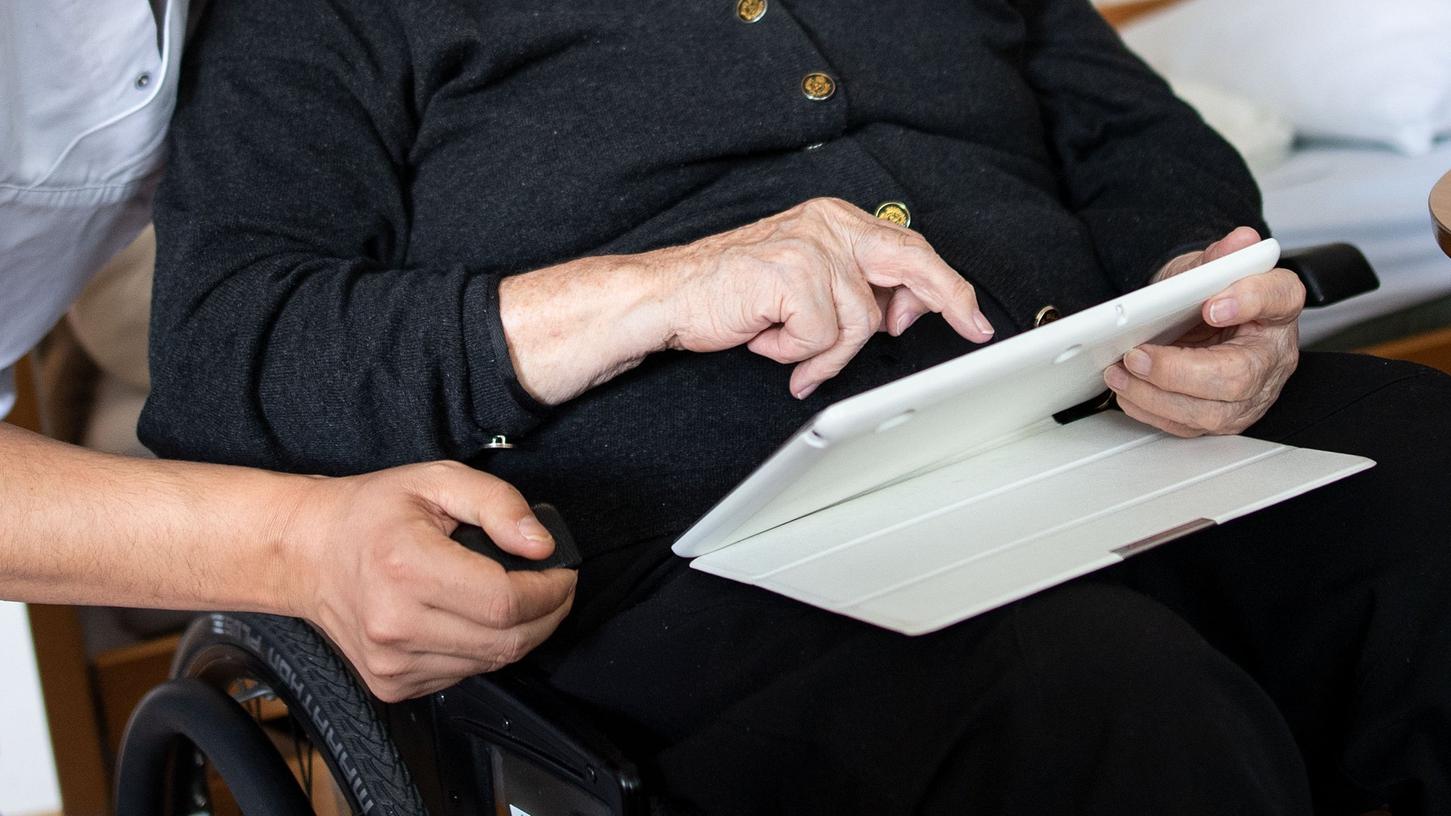 Ein Altenpfleger schaut in der Seniorenresidenz mit der Bewohnerin ein Video an.