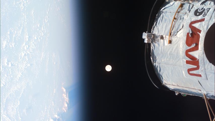 Ein Foto von Wartungsarbeiten an Hubble im Jahr 2008. Hier sieht man auch die Erde und dazwischen den Mond.